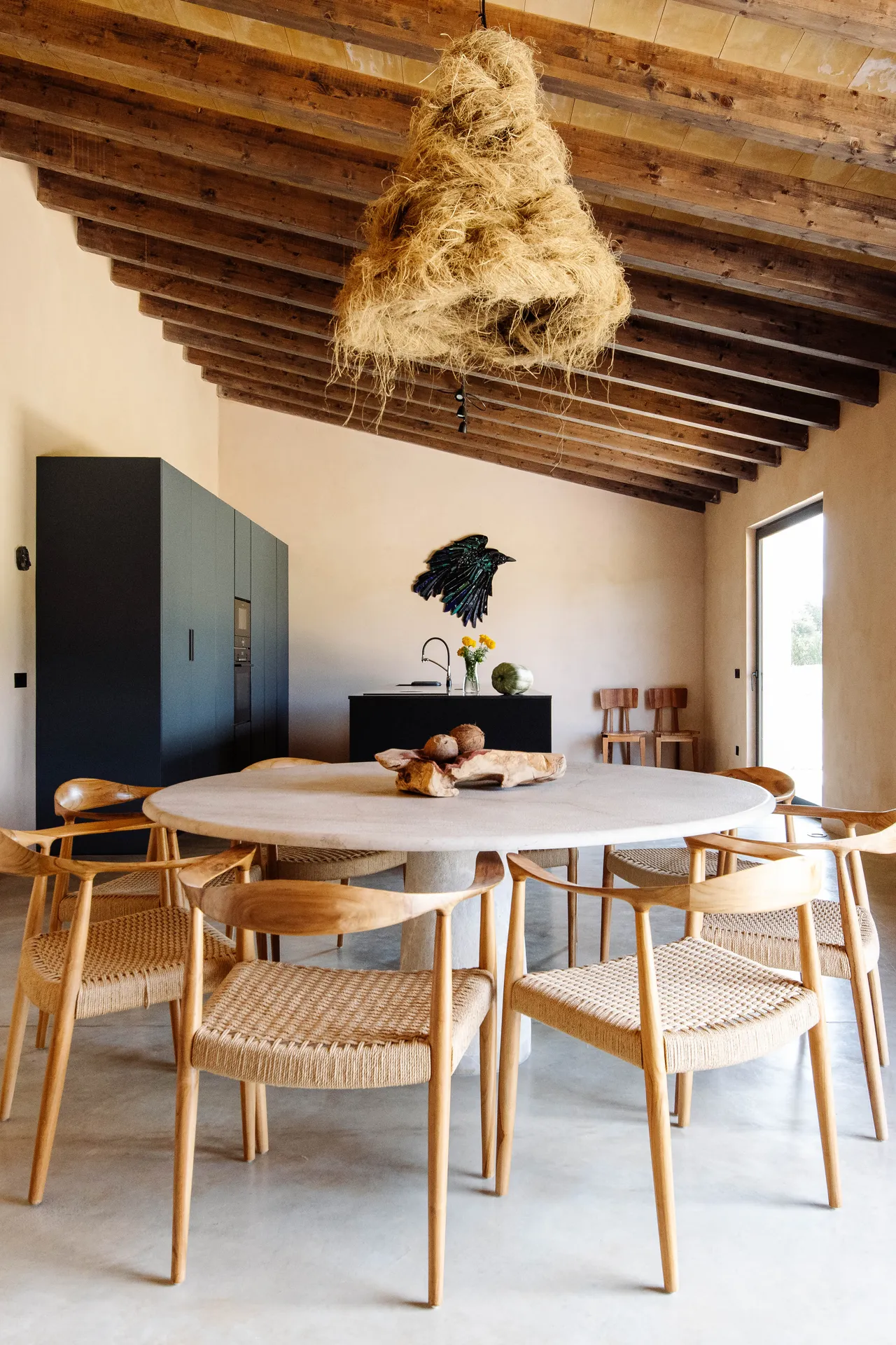 The dining room — round table, woven chairs and the sculptural hanging lamp in warm evening light