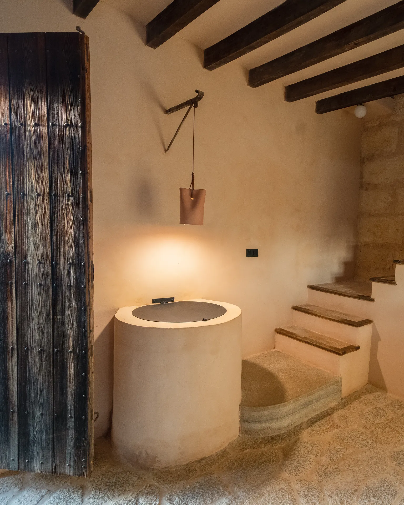 The entrance — original stone, old door, a round cistern and the staircase beyond