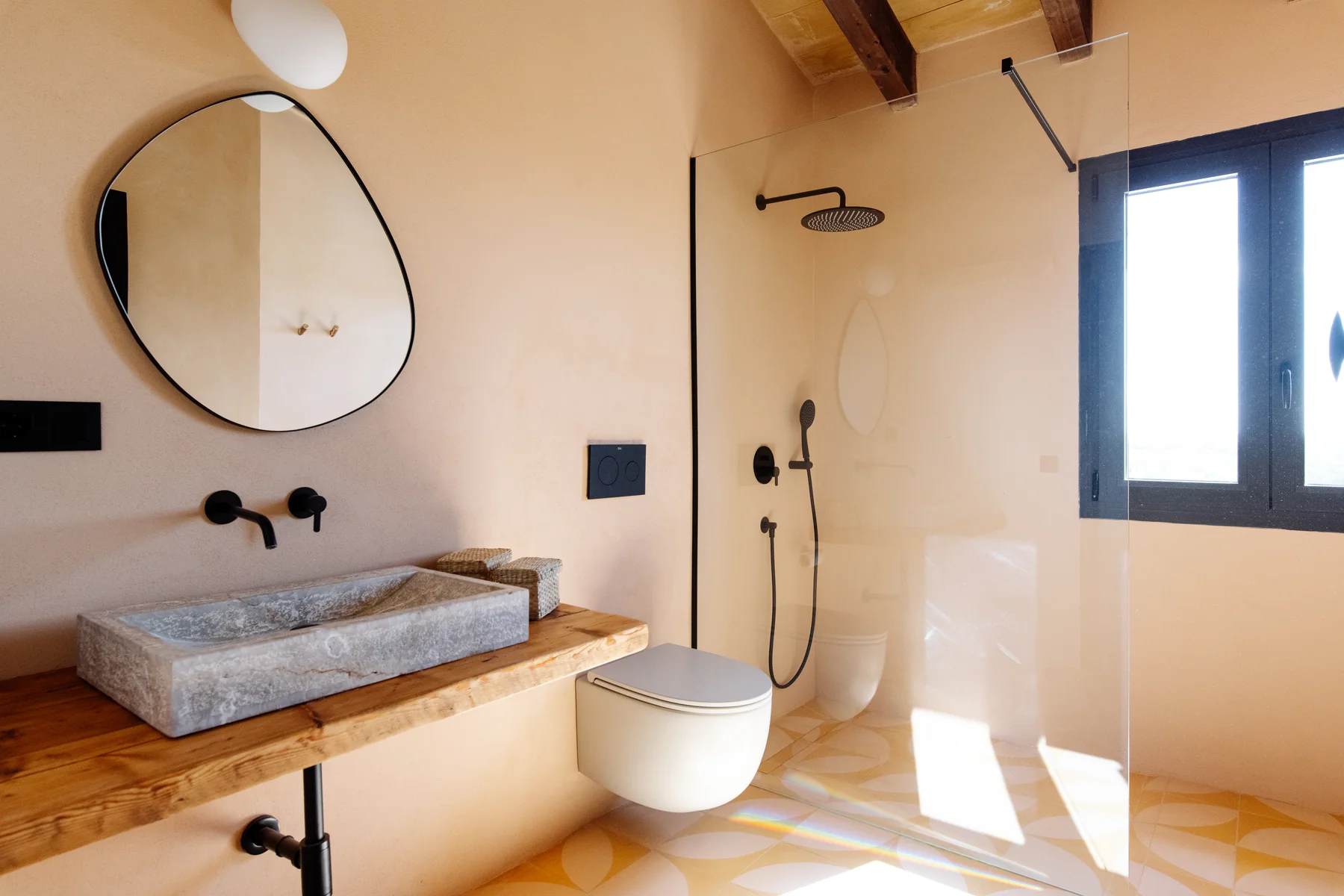 A bathroom — round mirror, stone sink and natural light through timber shutters