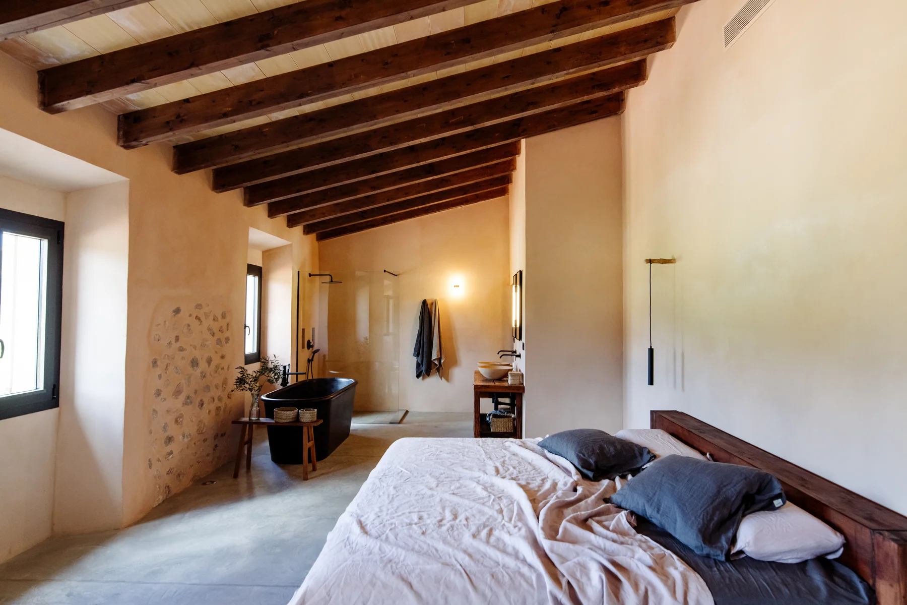 The master suite — king bed, stone wall and a freestanding black bathtub beyond