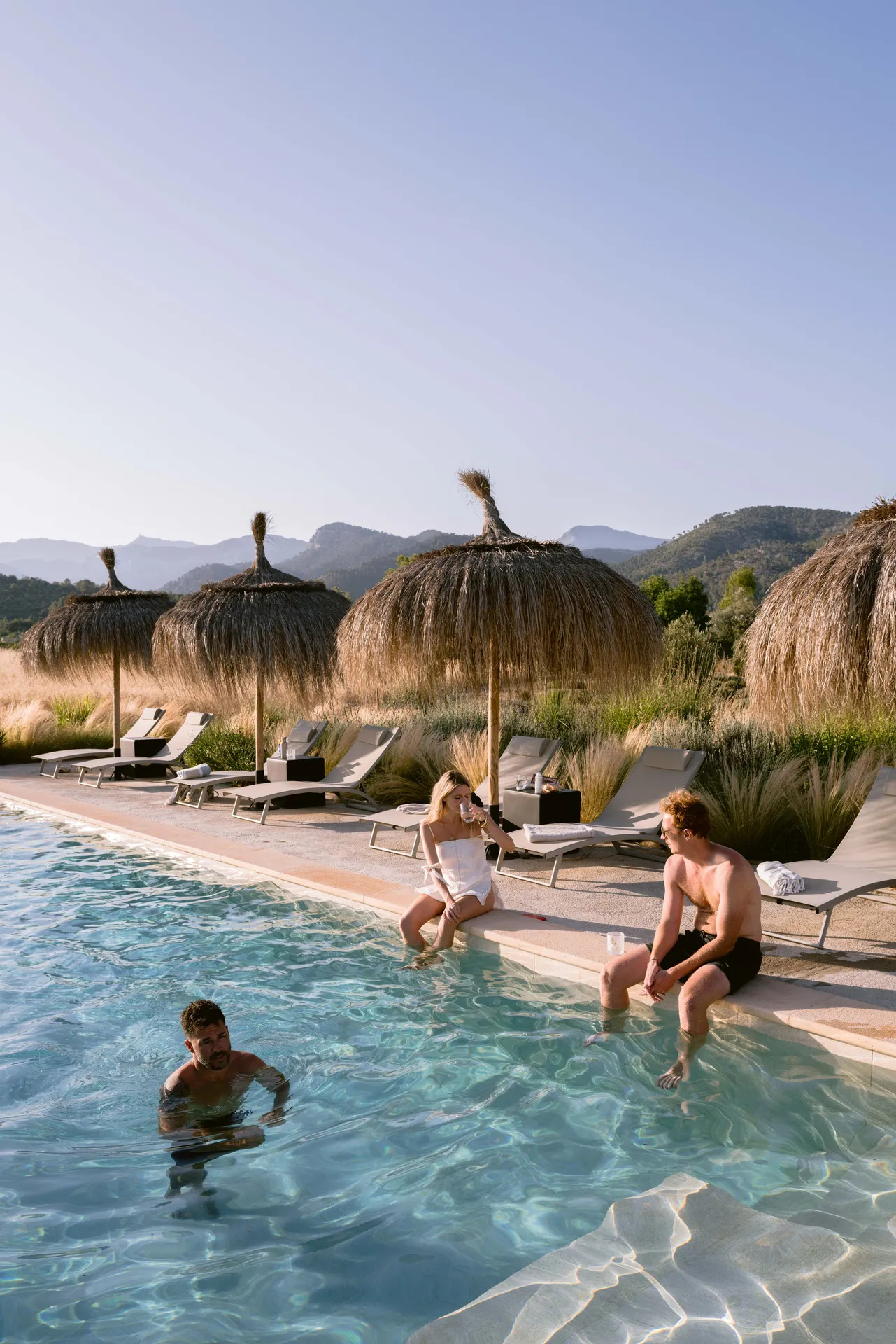 Friends at the pool — easy afternoons under the parasols with the Tramuntana behind
