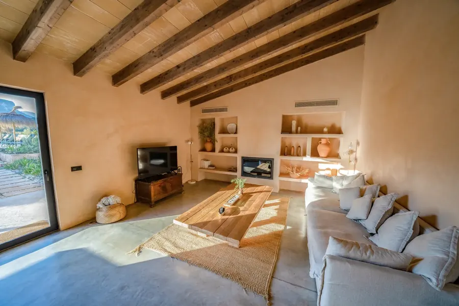 The living room in morning light — sofa, beams and open terrace door